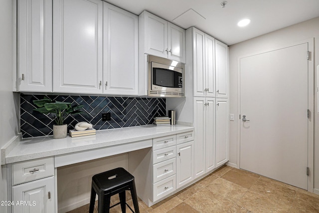 kitchen with decorative backsplash, stainless steel microwave, white cabinets, and built in study area