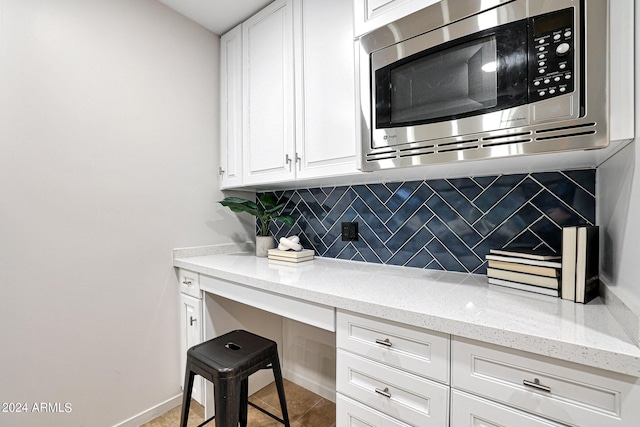 kitchen with stainless steel microwave, backsplash, baseboards, light stone countertops, and white cabinets