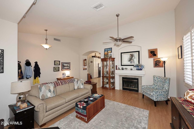 living room with arched walkways, light wood-style flooring, a tiled fireplace, and visible vents