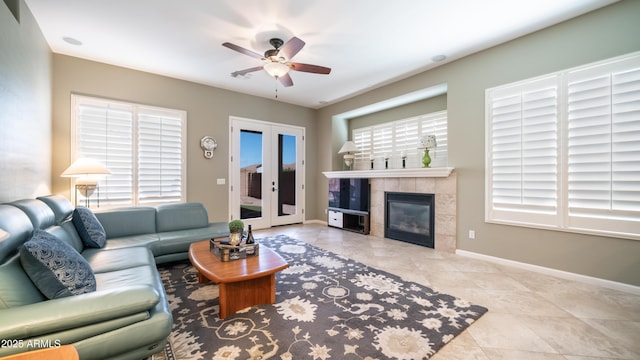 living room featuring baseboards, a ceiling fan, a tiled fireplace, and tile patterned flooring