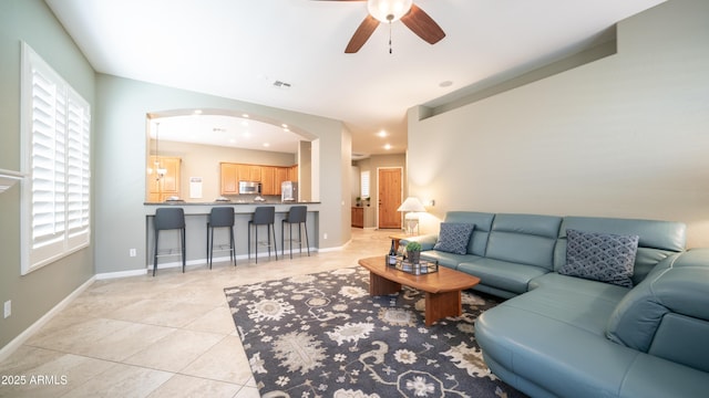 living area with light tile patterned floors, a ceiling fan, visible vents, baseboards, and arched walkways