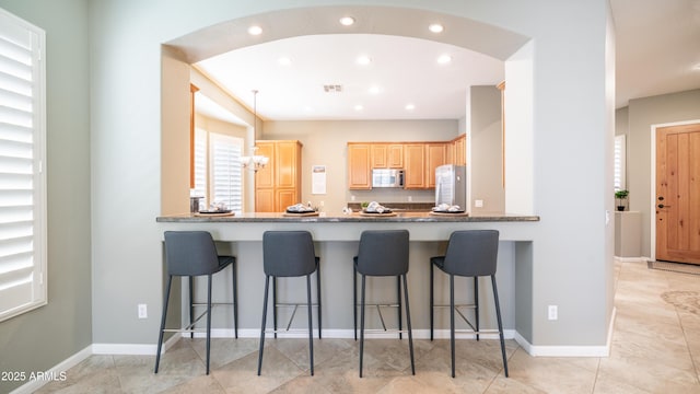 kitchen featuring arched walkways, stainless steel microwave, a peninsula, and freestanding refrigerator