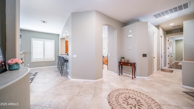 corridor with light tile patterned floors, visible vents, arched walkways, and baseboards