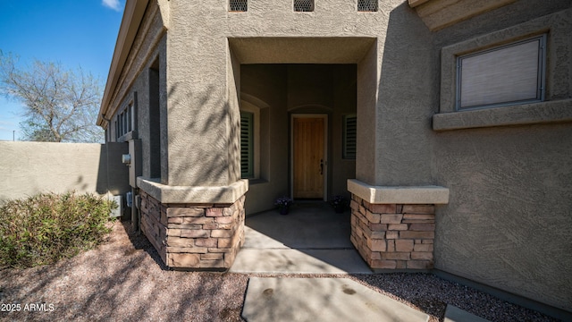 doorway to property featuring fence, stone siding, and stucco siding