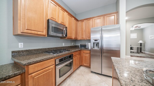 kitchen featuring a toaster, dark stone counters, light tile patterned floors, arched walkways, and stainless steel appliances