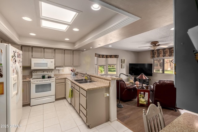 kitchen featuring a sink, a raised ceiling, a peninsula, white appliances, and open floor plan