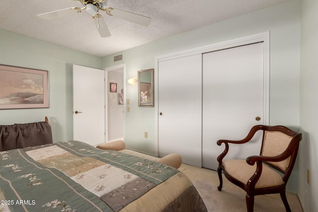 bedroom with a textured ceiling, carpet flooring, visible vents, ceiling fan, and a closet