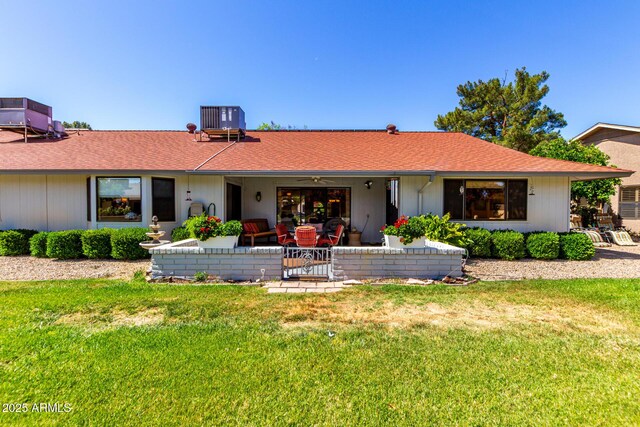 rear view of property with roof with shingles, cooling unit, and a lawn