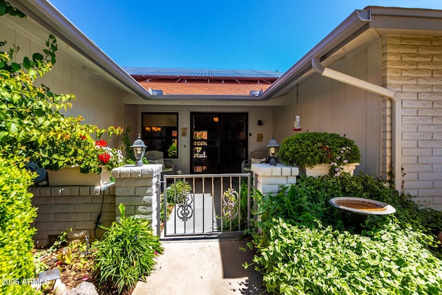doorway to property featuring a gate, roof mounted solar panels, and roof with shingles