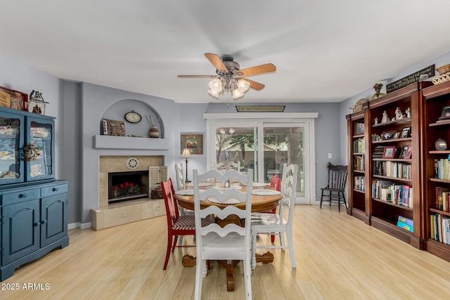 dining room with a tile fireplace, ceiling fan, and light hardwood / wood-style floors