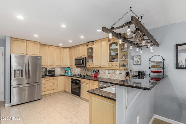 kitchen with light brown cabinets, appliances with stainless steel finishes, kitchen peninsula, dark stone counters, and backsplash