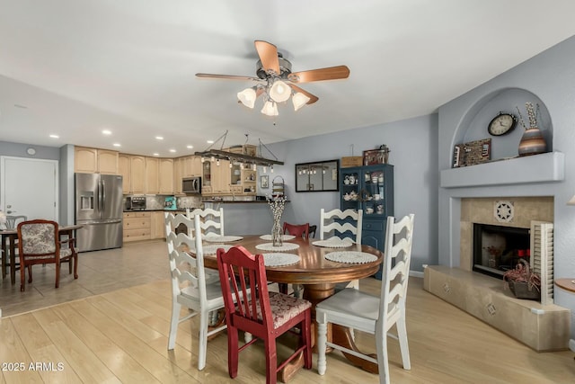 dining space featuring ceiling fan, a tiled fireplace, and light hardwood / wood-style floors