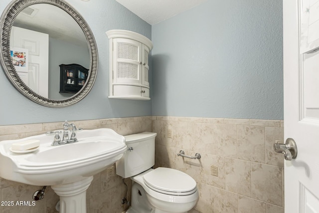 bathroom featuring toilet, sink, and tile walls