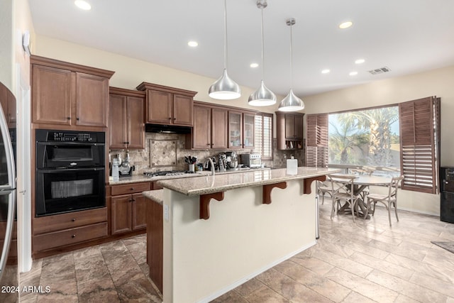 kitchen featuring a kitchen island with sink, a kitchen breakfast bar, hanging light fixtures, light stone counters, and stainless steel appliances