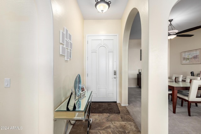 foyer featuring ceiling fan and dark colored carpet