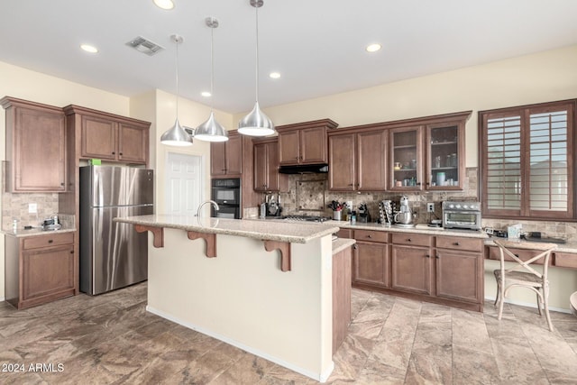 kitchen with pendant lighting, stainless steel fridge, an island with sink, tasteful backsplash, and a breakfast bar area