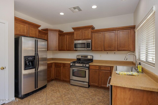 kitchen featuring appliances with stainless steel finishes, a sink, brown cabinetry, light tile patterned floors, and visible vents