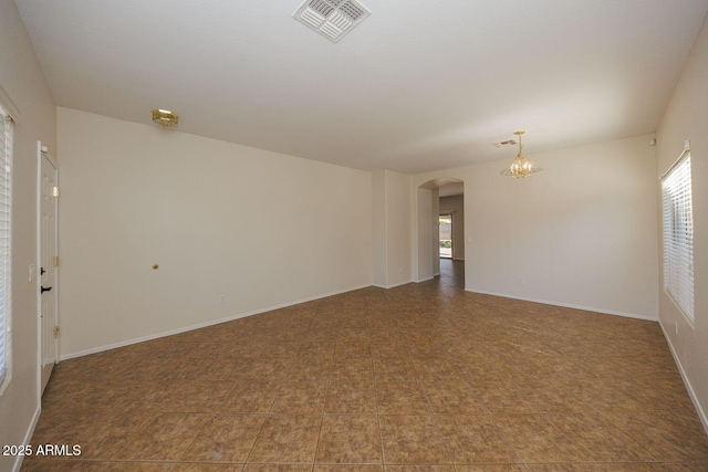 spare room featuring visible vents, arched walkways, baseboards, and a notable chandelier