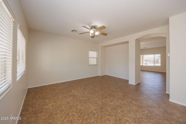 tiled empty room with visible vents, arched walkways, baseboards, and ceiling fan