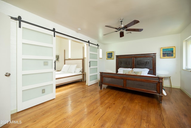 bedroom with a barn door, hardwood / wood-style floors, and ceiling fan