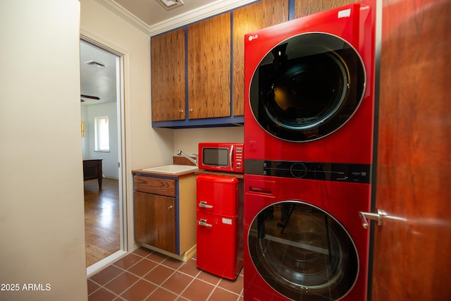 washroom with stacked washer / drying machine, sink, crown molding, cabinets, and tile patterned flooring