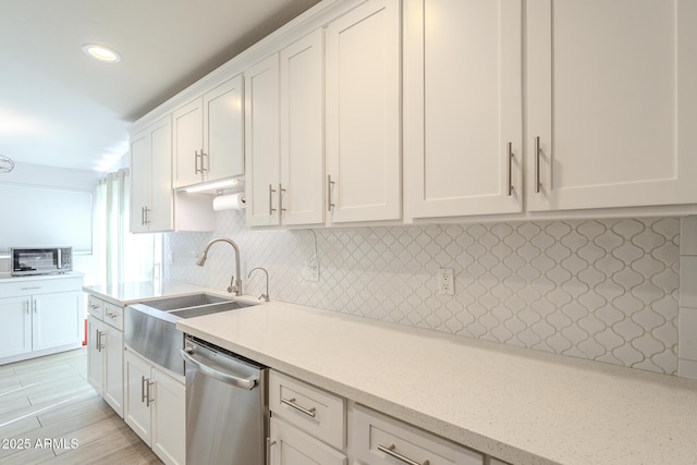 kitchen with backsplash, light stone countertops, dishwasher, white cabinetry, and a sink