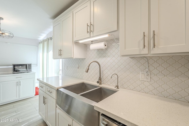 kitchen featuring tasteful backsplash, stainless steel microwave, light stone counters, white cabinetry, and a sink