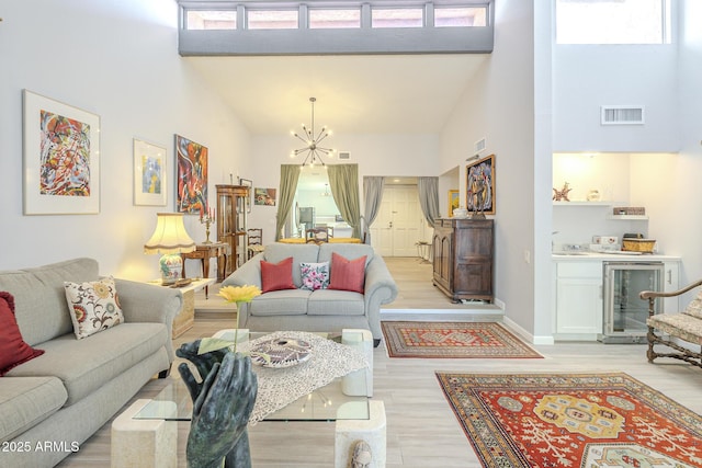 living room with light wood-type flooring, visible vents, beverage cooler, a high ceiling, and an inviting chandelier