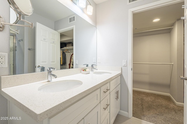 bathroom featuring a walk in closet, double vanity, visible vents, and a sink