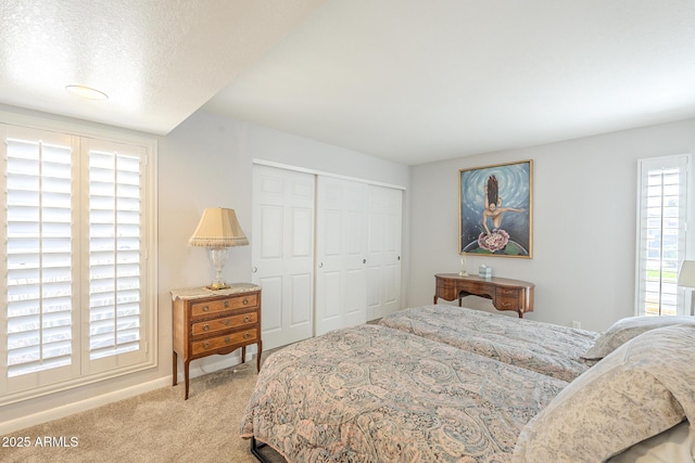 bedroom with a closet, light colored carpet, a textured ceiling, and baseboards