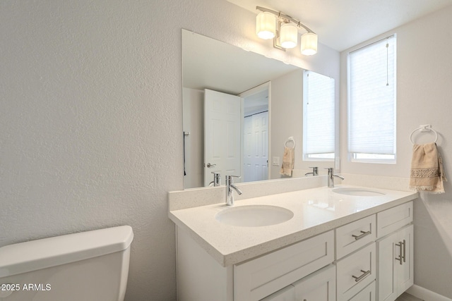 bathroom with double vanity, toilet, a textured wall, and a sink