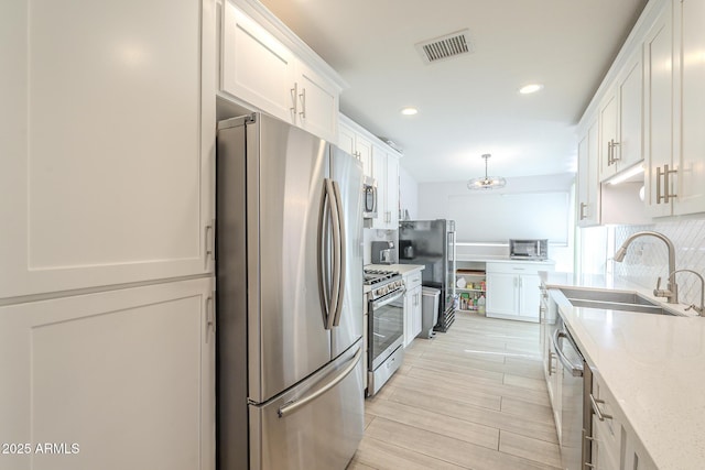 kitchen with visible vents, a sink, appliances with stainless steel finishes, white cabinets, and decorative backsplash