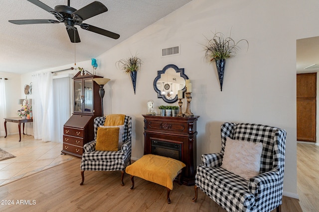 sitting room featuring lofted ceiling, ceiling fan, light hardwood / wood-style floors, and a textured ceiling