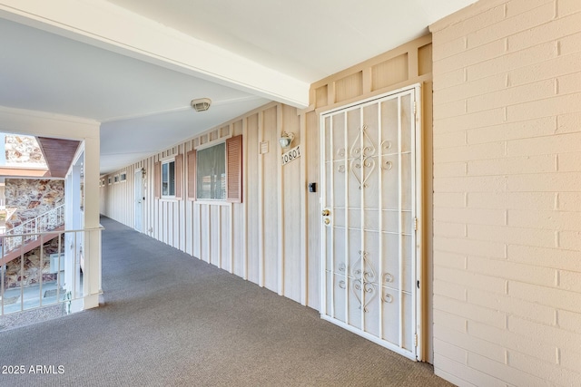 corridor with beam ceiling, carpet, and brick wall