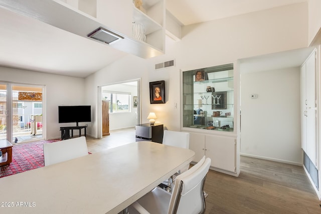 dining area with vaulted ceiling, visible vents, baseboards, and wood finished floors