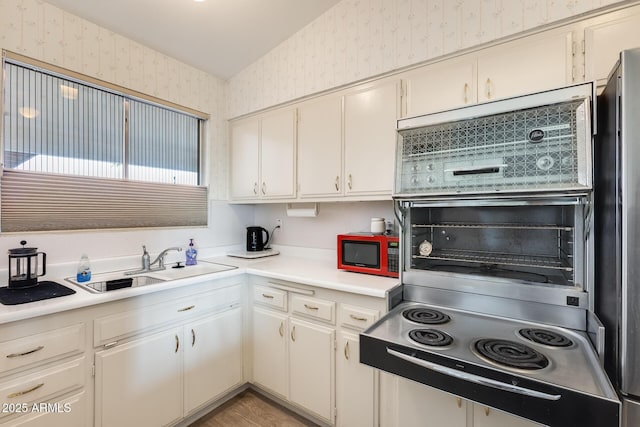 kitchen with a sink, light countertops, and wallpapered walls