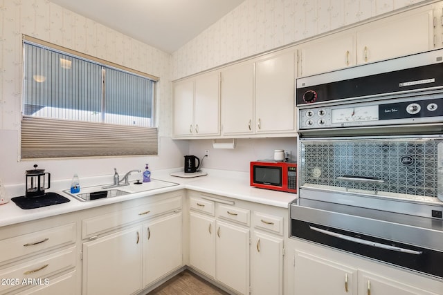 kitchen with oven, a sink, wallpapered walls, white cabinets, and light countertops