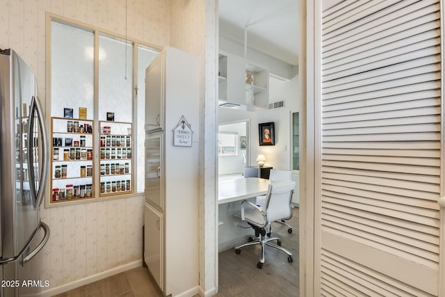 office area with wallpapered walls, wood finished floors, visible vents, and baseboards