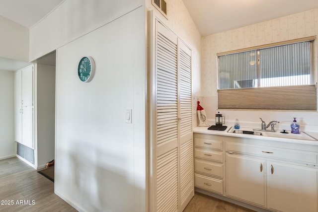 bathroom with a closet, wallpapered walls, baseboards, and wood finished floors