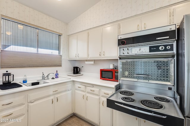 kitchen with a sink, freestanding refrigerator, light countertops, and wallpapered walls