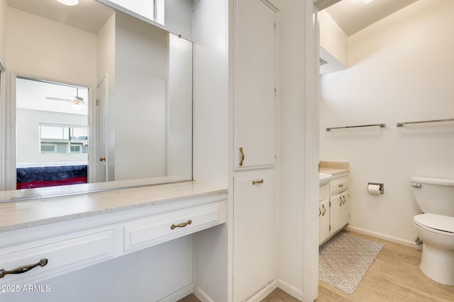 bathroom featuring toilet, wood finished floors, baseboards, ceiling fan, and vanity