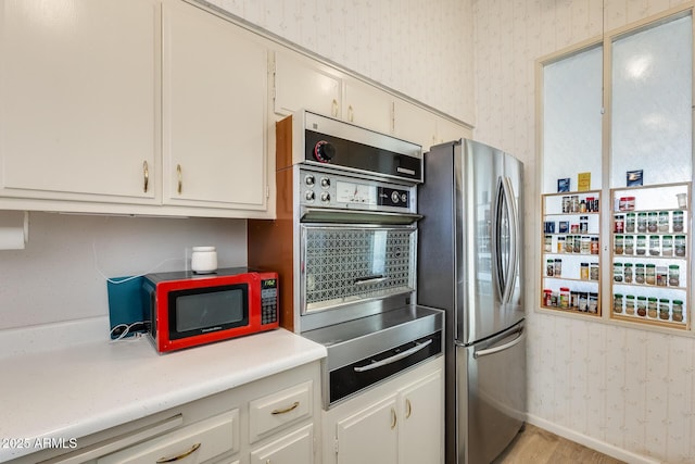 kitchen featuring baseboards, wallpapered walls, light countertops, white cabinets, and appliances with stainless steel finishes