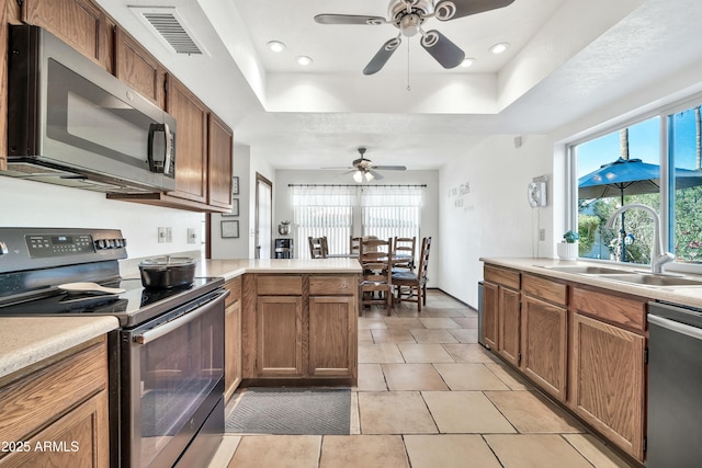 kitchen with sink, a raised ceiling, kitchen peninsula, and appliances with stainless steel finishes