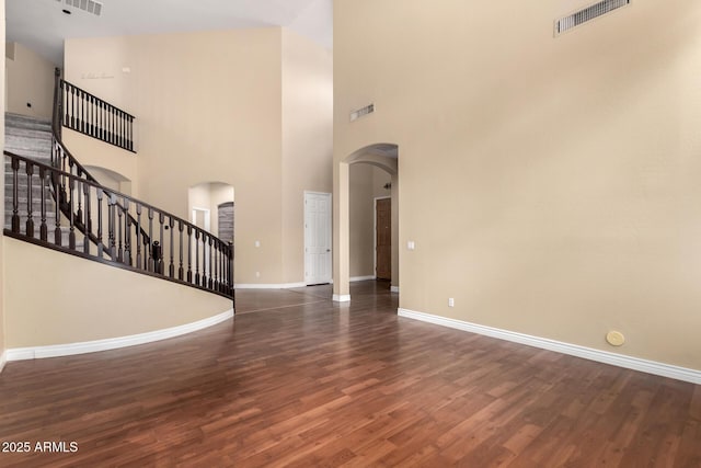 unfurnished living room with arched walkways, baseboards, stairs, wood finished floors, and a high ceiling