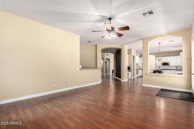 unfurnished living room featuring arched walkways, a ceiling fan, dark wood-type flooring, and baseboards