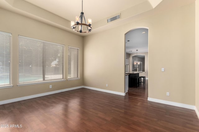 unfurnished room featuring arched walkways, a chandelier, dark wood-style floors, and baseboards