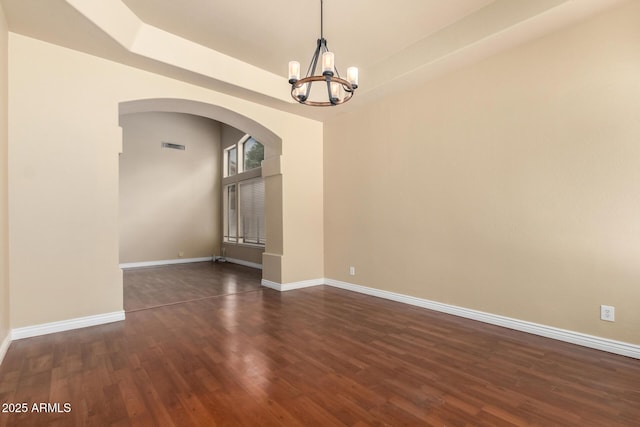 spare room with a chandelier, arched walkways, baseboards, and dark wood-type flooring