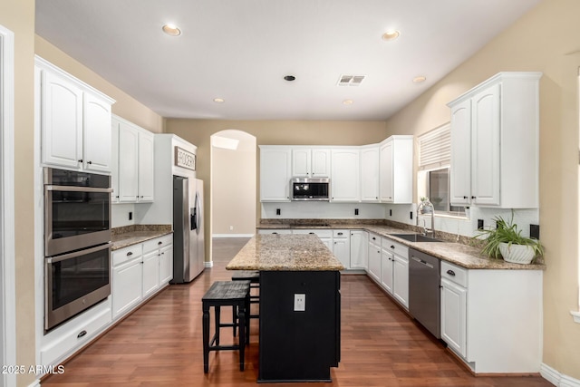 kitchen with stainless steel appliances, a sink, a center island, a kitchen breakfast bar, and white cabinetry