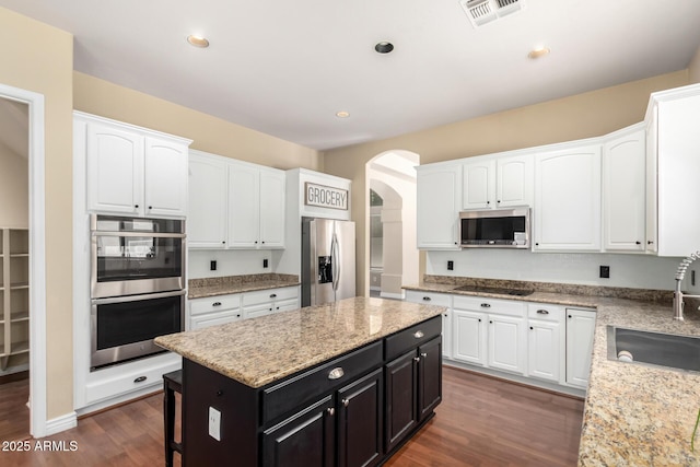 kitchen with stainless steel appliances, a sink, white cabinets, dark cabinetry, and recessed lighting