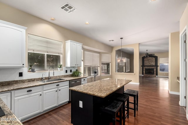 kitchen with a sink, white cabinets, dark wood finished floors, a kitchen island, and a stone fireplace